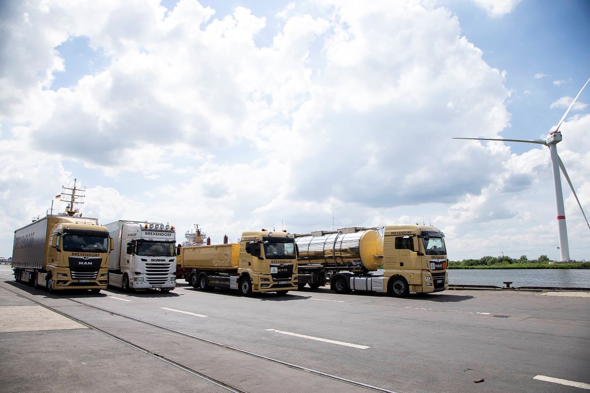 Drei nebeneinander geparkte Lastwagen in der Nähe einer Windkraftanlage bei bewölktem Himmel.